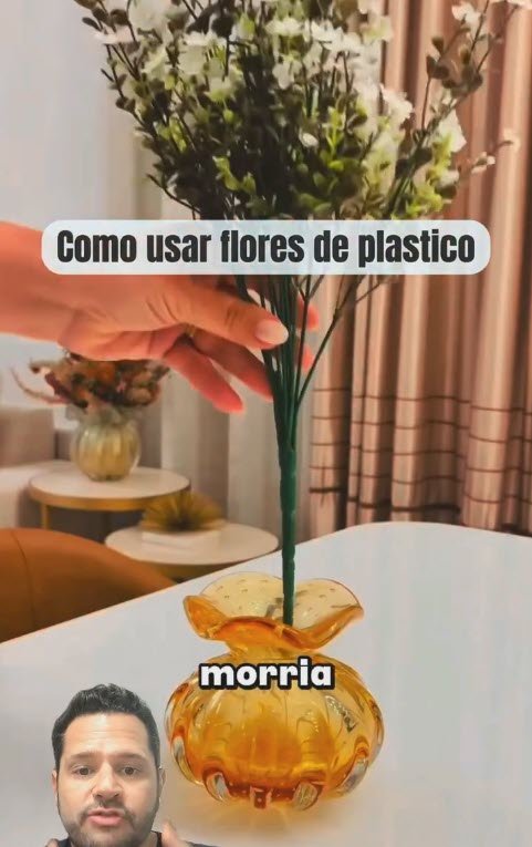 mão dobrando ramos de flores artificiais para baixo antes de colocar em vaso de vidro âmbar decorativo